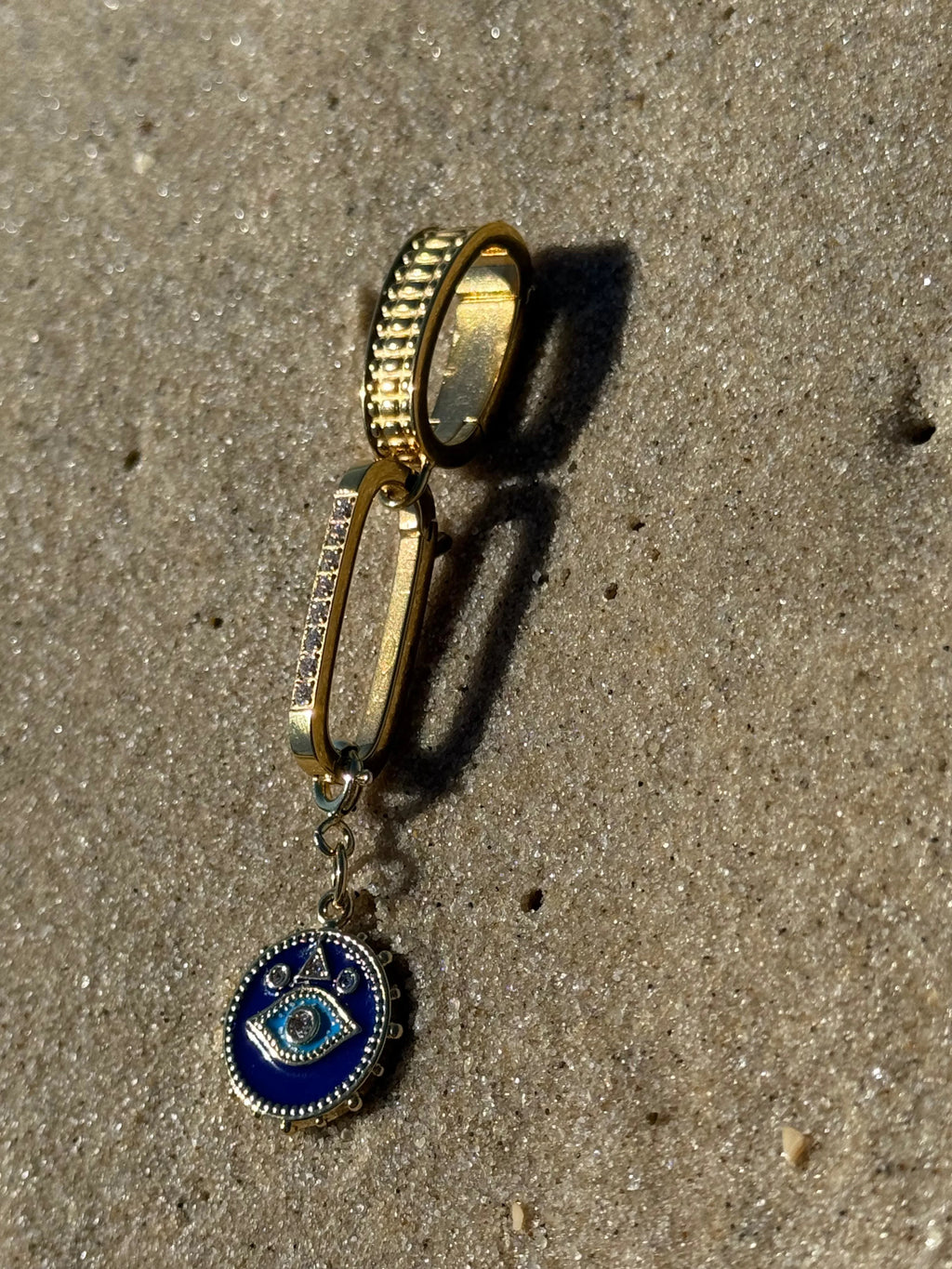 Gold ring with a blue pendant on a sandy surface
